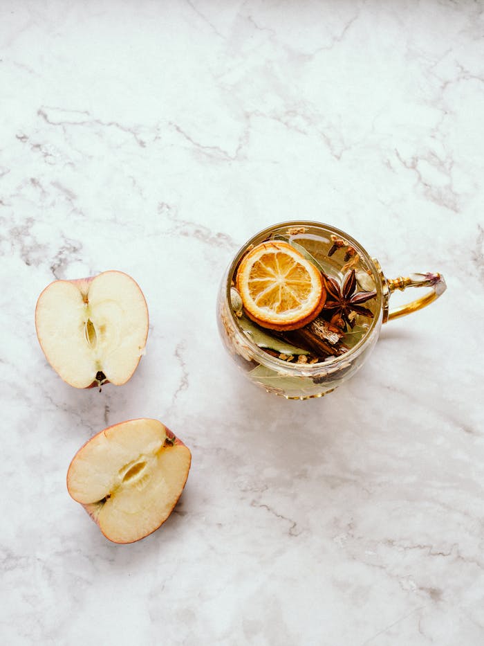 Flat lay of herbal tea with apple slices, dried lemon, and star anise on marble.