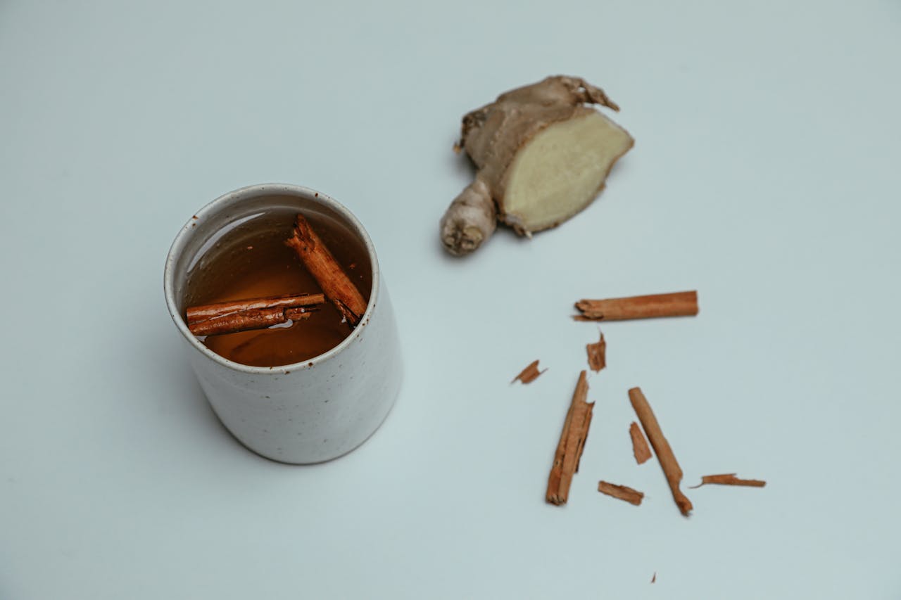 A cup of tea infused with cinnamon sticks and ginger on a white background.