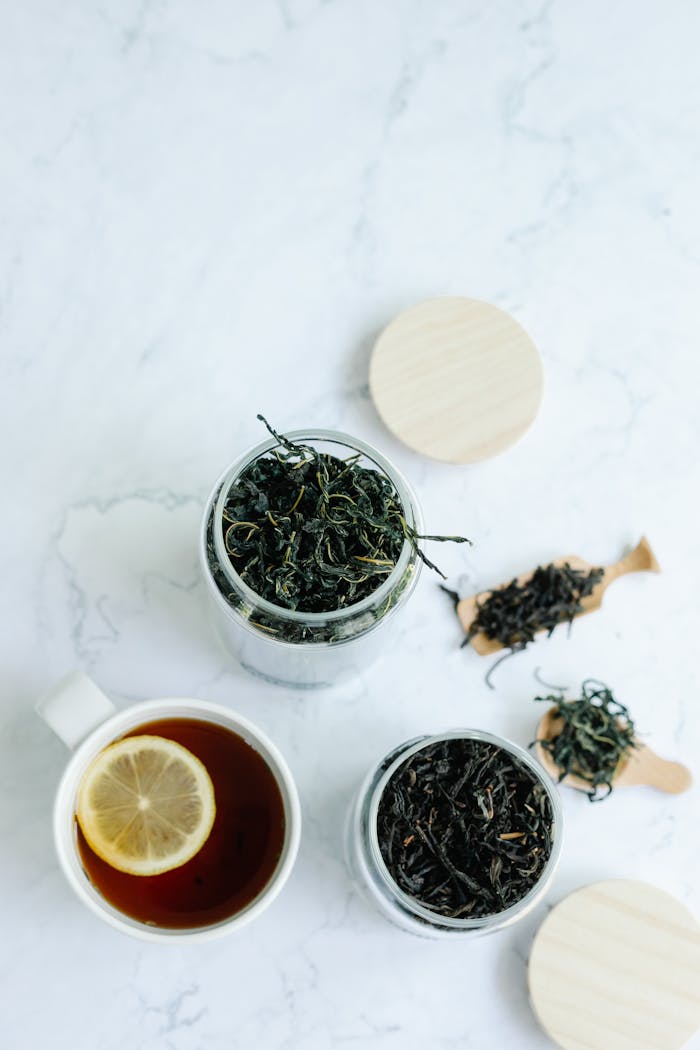Aerial view of herbal tea with jars and a lemon slice on a white background.